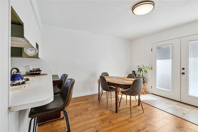 dining area with light wood finished floors, french doors, a textured ceiling, and baseboards