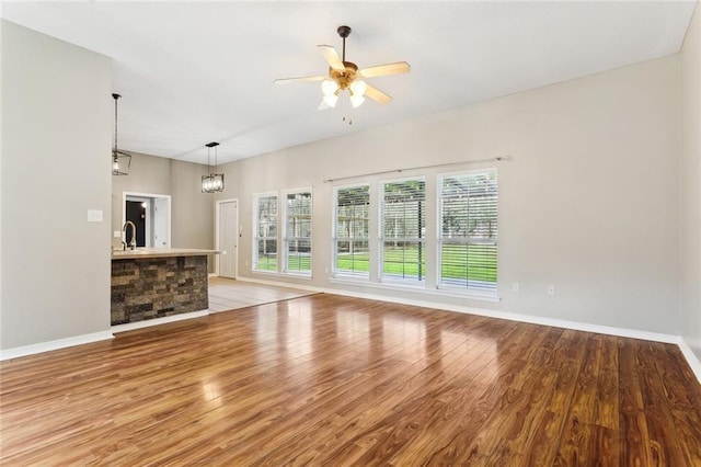 unfurnished living room with light wood-style floors, baseboards, and a ceiling fan