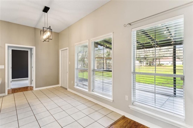 unfurnished dining area featuring light tile patterned flooring, a notable chandelier, and baseboards