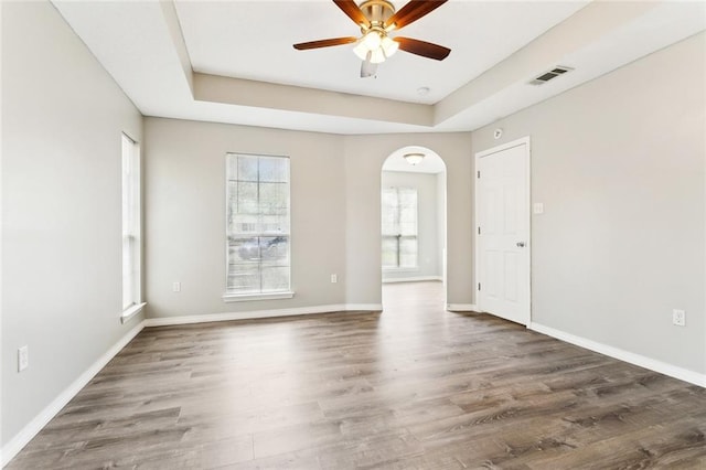 spare room featuring dark wood-style floors, a raised ceiling, visible vents, and baseboards