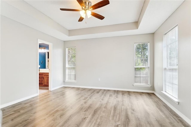 empty room with light wood-style floors, a raised ceiling, and baseboards