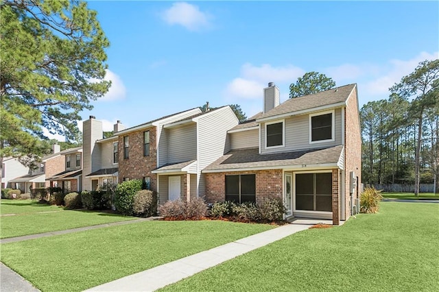 townhome / multi-family property featuring a front yard, entry steps, a chimney, and brick siding