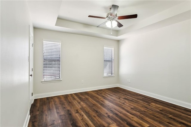 empty room featuring baseboards, a tray ceiling, and dark wood-style flooring