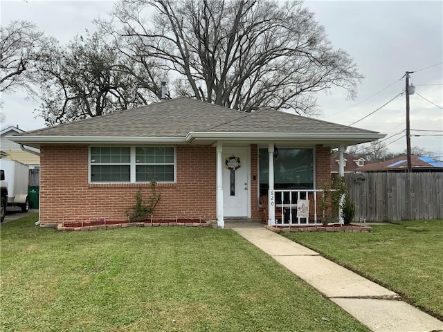 bungalow-style house with a shingled roof, a front yard, fence, and brick siding