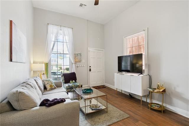 living room with dark wood-style floors, a high ceiling, visible vents, and baseboards