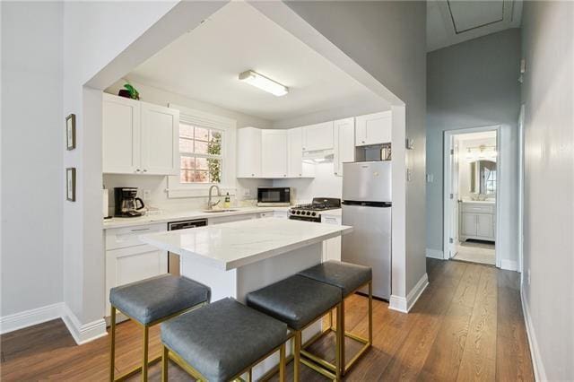 kitchen featuring white cabinets, stove, a center island, freestanding refrigerator, and a sink