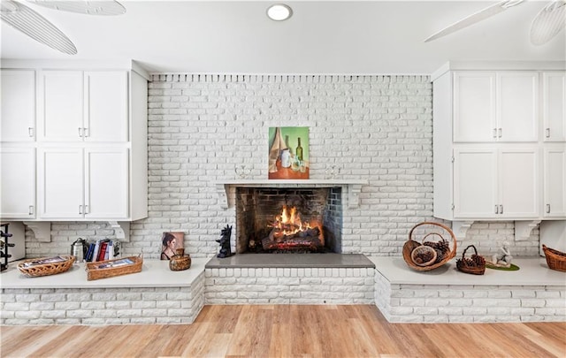 kitchen featuring light wood finished floors, a brick fireplace, white cabinetry, and light countertops