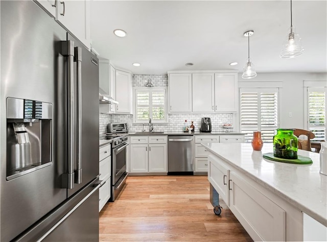 kitchen with pendant lighting, stainless steel appliances, a wealth of natural light, white cabinetry, and a sink