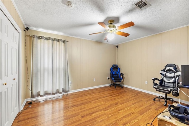 unfurnished room featuring a textured ceiling, ornamental molding, wood finished floors, and visible vents