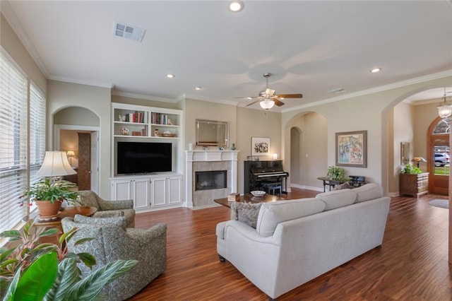 living room with visible vents, arched walkways, a tile fireplace, ornamental molding, and dark wood-type flooring