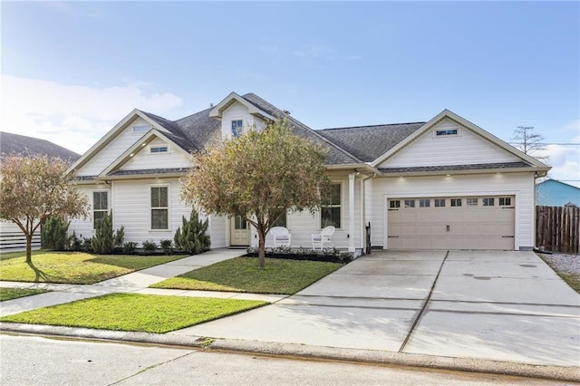 view of front of house featuring roof with shingles, concrete driveway, an attached garage, a front yard, and fence