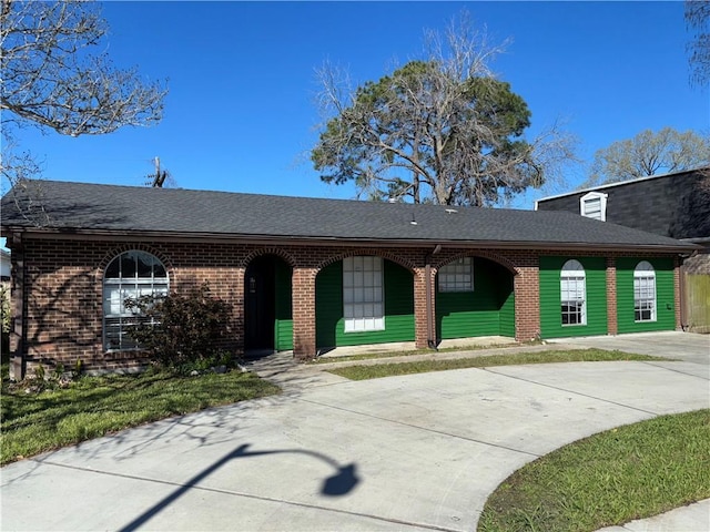 view of front of property featuring a front yard, brick siding, driveway, and roof with shingles