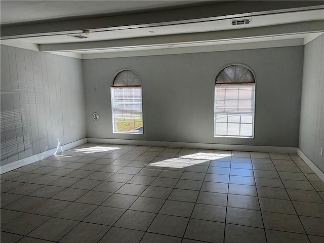 empty room featuring beamed ceiling, tile patterned flooring, visible vents, and baseboards