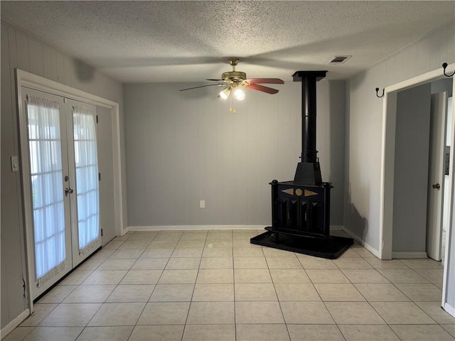 unfurnished living room featuring french doors, light tile patterned floors, visible vents, a wood stove, and a textured ceiling