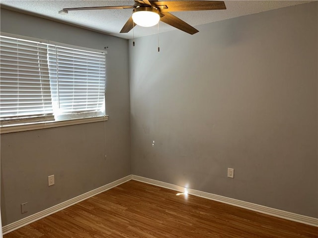 unfurnished room with a textured ceiling, wood finished floors, a ceiling fan, and baseboards