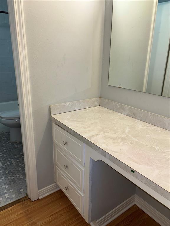 bathroom featuring baseboards, toilet, wood finished floors, walk in shower, and vanity