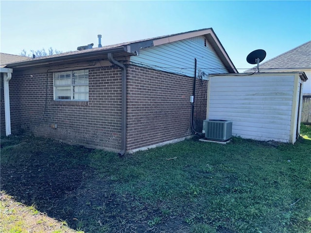 view of side of home with a lawn, central AC, and brick siding