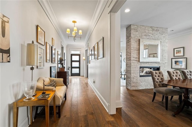 hall with an inviting chandelier, baseboards, ornamental molding, and dark wood-style flooring