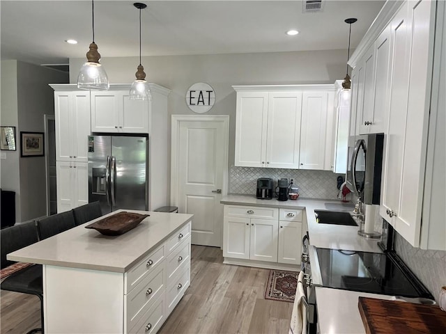 kitchen featuring stainless steel appliances, light countertops, white cabinetry, and pendant lighting