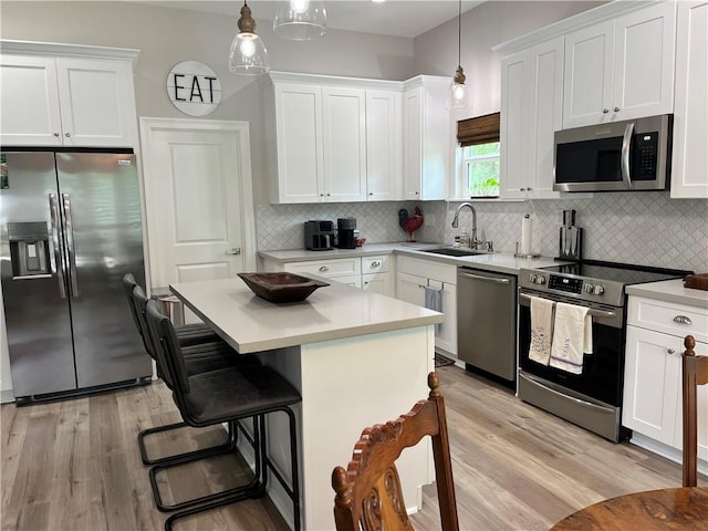 kitchen featuring white cabinets, hanging light fixtures, stainless steel appliances, light countertops, and a sink