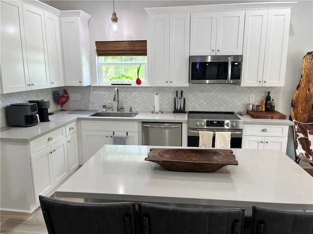 kitchen with stainless steel appliances, a sink, white cabinets, light countertops, and decorative light fixtures