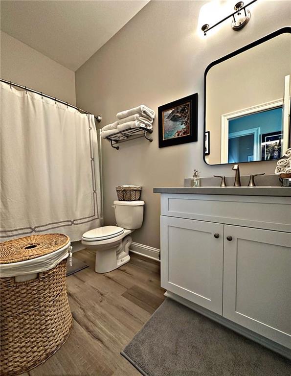 bathroom featuring toilet, a shower with shower curtain, wood finished floors, vanity, and baseboards