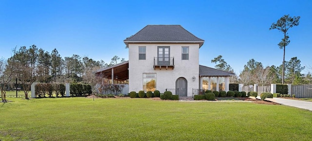 view of front of home with a balcony, stucco siding, fence, and a front yard