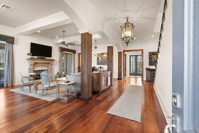 foyer with visible vents, arched walkways, dark wood-style flooring, a fireplace, and ceiling fan with notable chandelier