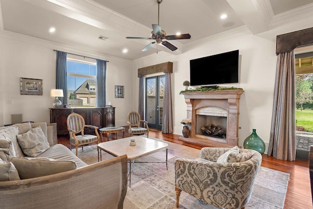 living room featuring a fireplace with raised hearth, recessed lighting, visible vents, ornamental molding, and light wood-type flooring