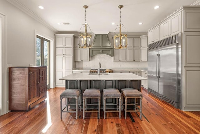 kitchen with visible vents, an island with sink, decorative light fixtures, stainless steel built in fridge, and custom exhaust hood