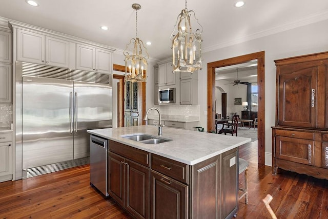 kitchen with dark wood finished floors, decorative backsplash, built in appliances, pendant lighting, and a sink