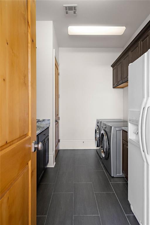 laundry room featuring dark tile patterned floors, washing machine and dryer, visible vents, and baseboards