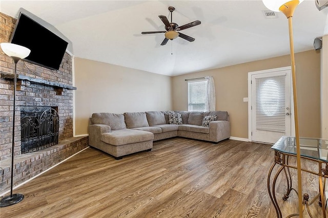 living area featuring a fireplace, visible vents, a ceiling fan, vaulted ceiling, and wood finished floors