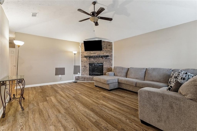 living room featuring ceiling fan, wood finished floors, visible vents, vaulted ceiling, and a brick fireplace