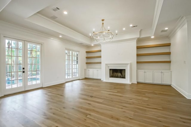 unfurnished living room with light wood finished floors, ornamental molding, french doors, a fireplace, and a raised ceiling