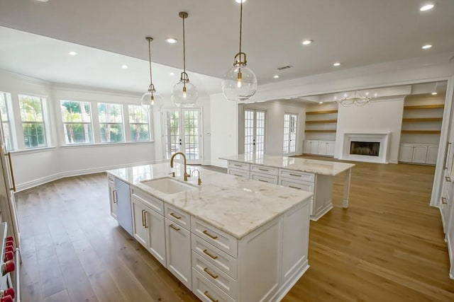 kitchen featuring a kitchen island with sink, open floor plan, wood finished floors, white cabinetry, and a sink