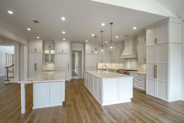 kitchen with custom exhaust hood, a spacious island, light wood-type flooring, and visible vents