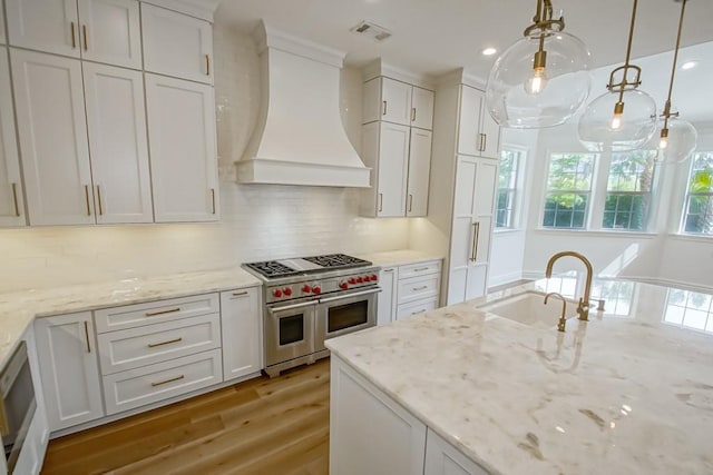 kitchen with double oven range, visible vents, premium range hood, a sink, and backsplash