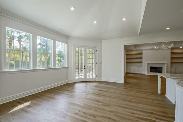 unfurnished living room with a fireplace, wood finished floors, crown molding, and french doors