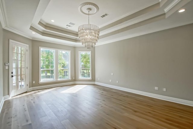 empty room with visible vents, ornamental molding, wood finished floors, baseboards, and a raised ceiling