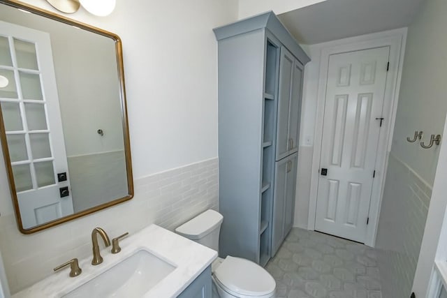 bathroom featuring wainscoting, toilet, tile walls, and vanity