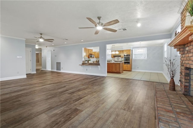 unfurnished living room with light wood finished floors, visible vents, a ceiling fan, crown molding, and a fireplace