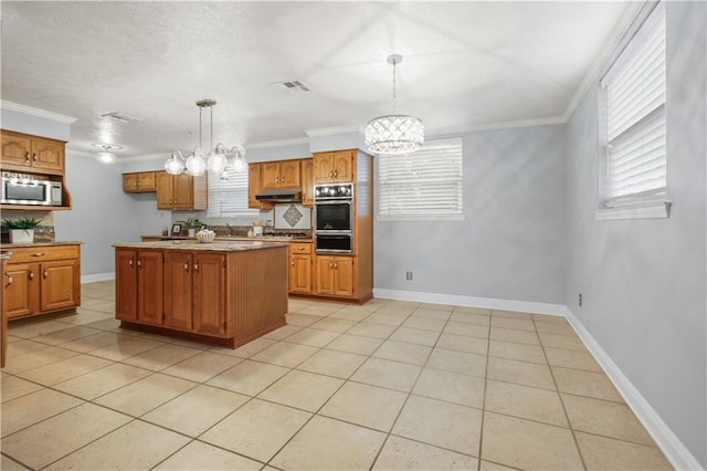 kitchen with pendant lighting, a kitchen island, appliances with stainless steel finishes, brown cabinetry, and an inviting chandelier