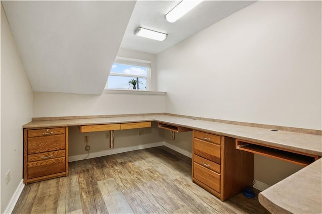 office space with light wood-style floors, lofted ceiling, and built in desk