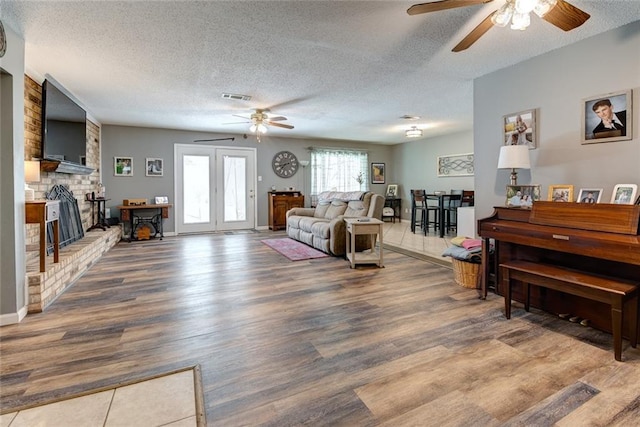 living room featuring a textured ceiling, a fireplace, wood finished floors, visible vents, and baseboards