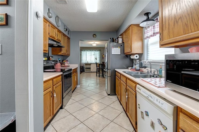 kitchen featuring stainless steel appliances, light countertops, under cabinet range hood, a sink, and light tile patterned flooring