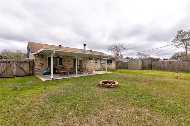 back of house with brick siding, a patio, a storage shed, an outdoor fire pit, and a fenced backyard