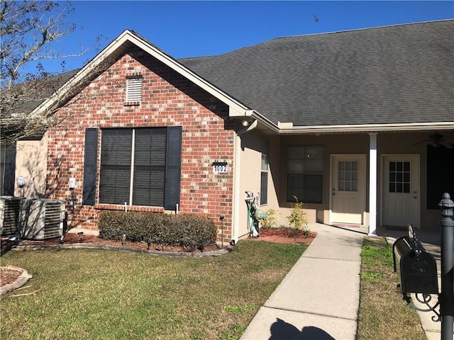 view of front of home featuring central AC unit, brick siding, a front yard, and a ceiling fan