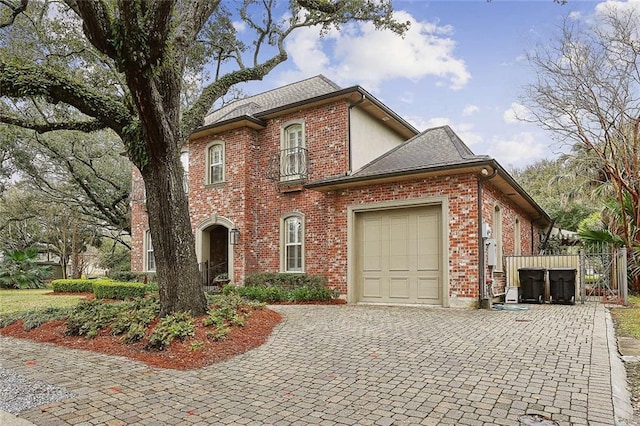 traditional-style house featuring decorative driveway, brick siding, an attached garage, and roof with shingles