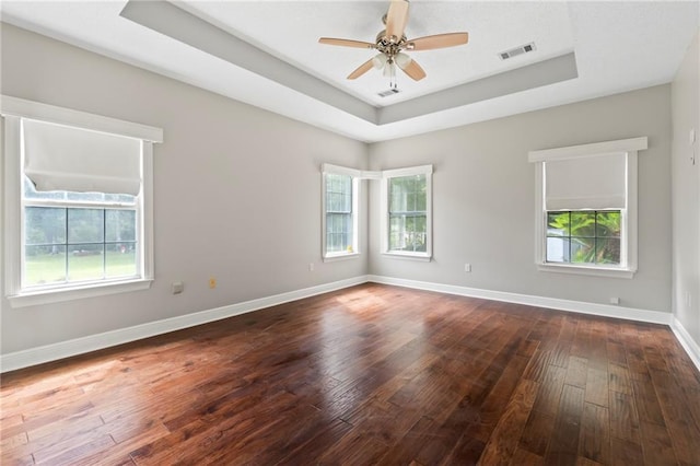 empty room with dark wood-style flooring, a raised ceiling, visible vents, and baseboards